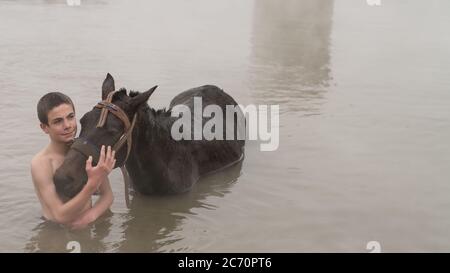 Guroymak, Bitlis, Türkei - Februar 2020: Kleiner Junge und sein Pferd im Thermalwasser, Freundschaft mit Haustieren, Tierdusche Stockfoto