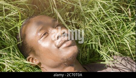 Friedlicher afroamerikanischer Kerl, der sich in der Sonne entspannt und auf dem Gras liegt Stockfoto