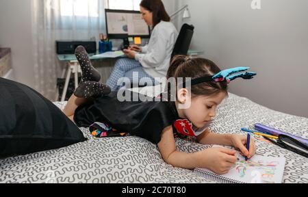 Mädchen Zeichnung in Verkleidung während ihre Mutter Telearbeit Stockfoto