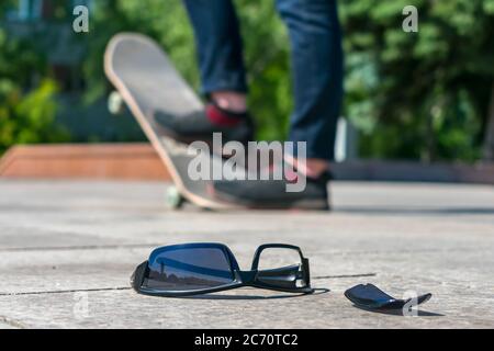 Verlorene schwarze Brille liegt auf der Straße vor dem Hintergrund eines Mannes, der auf einem Skateboard Schlittschuh läuft Stockfoto