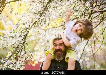 Frühling. Hipster Huckepack Baby. Bärtiger brutaler Mann guter Vater. Vater und Sohn. Bester Vater aller Zeiten. Vatertag. Kind, das Spaß mit Papa hat. Frohe Familie. Kleiner Junge und Vater im Hintergrund Natur. Stockfoto