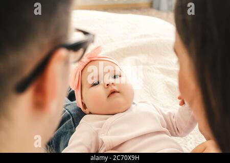 Köpfe von Vater, Mutter und niedlichen Baby dazwischen, Familie liegen auf hellem Bett. Stockfoto