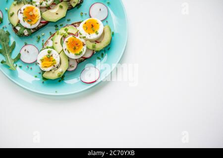 Sandwiches mit weich gekochtem Ei, Avocado, Rettich, Rucola, grüne Zwiebel und Leinsamen auf blauem Teller. Gesunde Snacks. Stockfoto