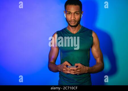 Fitness Guy Mit Mobiltelefon Tragen Von Ohrstöpseln, Blauer Hintergrund, Studio Stockfoto