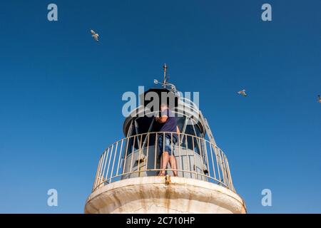 Mario Sanz schützt sich vor den Möwenangriffen mit einem Regenschirm, während er die Fenster des Leuchtturms La Garrucha in Spanien reinigt. Datum: 07/06/2017. Stockfoto