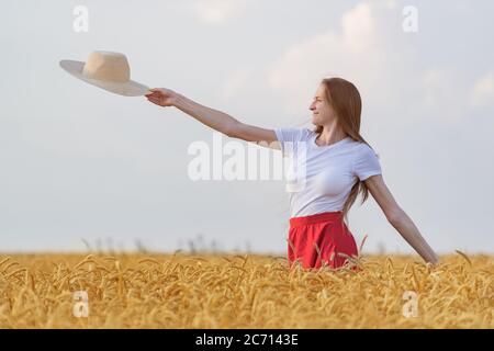 Junge Frau steht mitten im Feld des reifen Weizens und hält Strohhut. Stockfoto