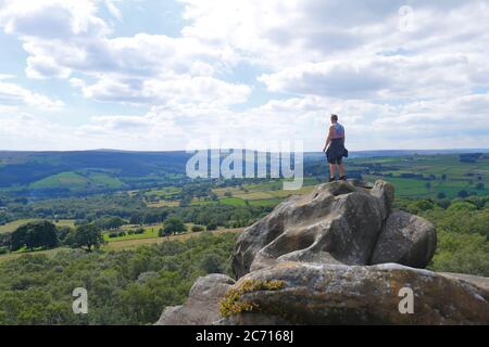 Ein Tourist nimmt die Sehenswürdigkeiten der Yorkshire Dales von einer der vielen Felsformationen in Brimham Rocks, die von der National Trust gehört. Stockfoto