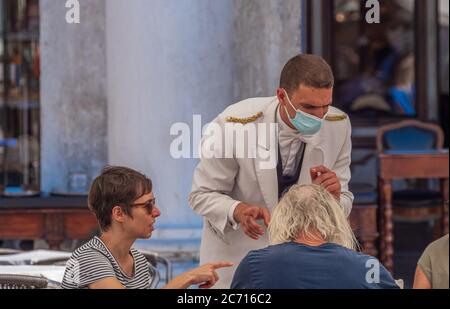 Kellner am Markusplatz in Venedig mit Gesichtsmaske, um die Gäste vor einer Infektion mit dem Corona-Virus zu schützen. Stockfoto