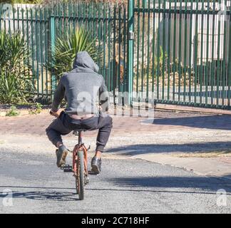 Alberton, Südafrika - unidentifizierte schwarze Jugendliche fährt ein kleines Fahrrad in einem öffentlichen Straßenbild im Querformat Stockfoto