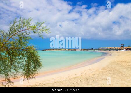 Griechenland. Kreta. 22.06.2020. Strand mit Sonnenschirmen, rosa Sand, grünen Baum und türkisfarbenem Wasser und Wolken in blauen Himmel. Stockfoto
