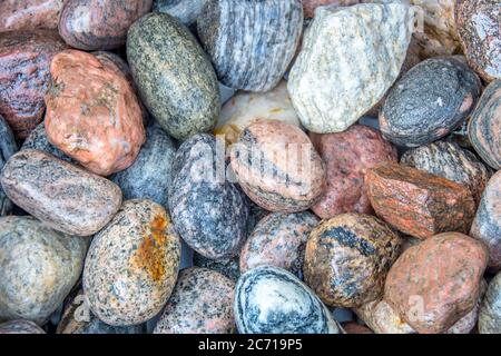 Nahaufnahme von hellen Farben und schönen Mustern einer Sammlung von glatten nassen Flussfelsen in einer Outdoor-Umgebung in verschiedenen Formen und Größen. Stockfoto