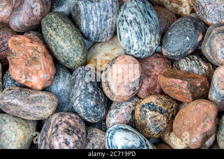 Nahaufnahme von hellen Farben und schönen Mustern einer Sammlung von glatten nassen Flussfelsen in einer Outdoor-Umgebung in verschiedenen Formen und Größen. Stockfoto