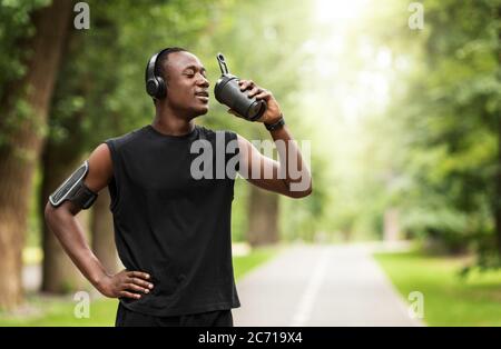 Athletischer schwarzer Mann, der Protein trinkt, während er im Park trainiert Stockfoto
