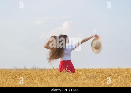 Schöne Mädchen geht auf Feld und genießen sonnigen Tag. Junge Frau hält Hut vor Weizenfeld Hintergrund. Stockfoto