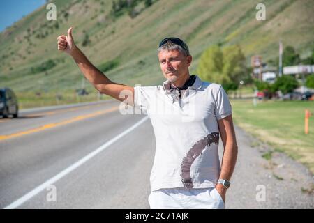 Außenaufnahme eines Reisemannes, der in einem lässigen T-Shirt entlang einer Landstraße trampelt. Reise-, Tourismus- und Urlaubskonzept. Stockfoto