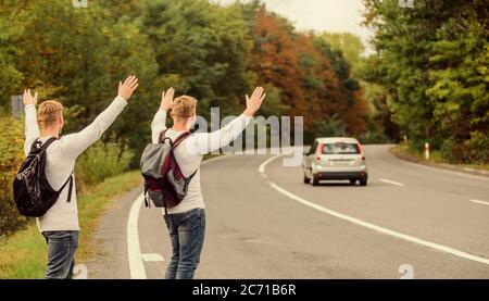 Nur Freunde und Straße voran. das Gefühl der Freiheit. Mit Freunden unterwegs. Anreise per Autostop. Hoffnungslos hitchhiker. Männer versuchen stop Auto. Zwillinge zu Fuß entlang der Straße. Wanderer Mann auf der Straße. Art des Reisens. Stockfoto