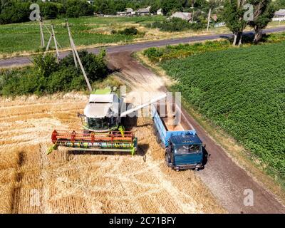 Aerial Drohne Draufsicht große leistungsstarke industrielle Mähdrescher Maschine Entladen bin von Weizen Getreidefeld in LKW auf hellen Sommer oder Tag Stockfoto