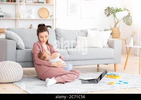 Pflege Mutter Pflege Baby während der Arbeit mit Laptop und Papiere zu Hause Stockfoto