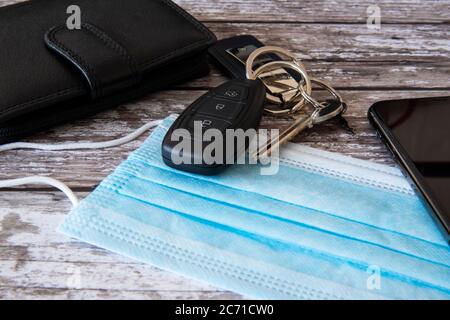 Stillleben zeigt wesentliche Elemente mit Ihnen, wenn Sie das Haus verlassen. Geld, Schlüssel, Telefon und jetzt eine Gesichtsmaske Stockfoto
