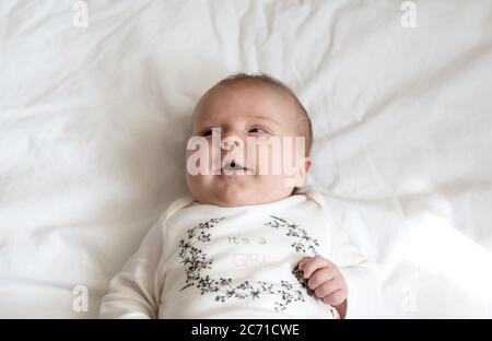 Ein Nahaufnahme Porträt eines kleinen Mädchens, das im Bett liegt und lächelt. Drei Monate altes Mädchen in gelben Kleidern lacht Stockfoto