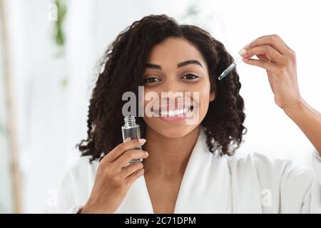 Hautpflegeprodukte. Lächelnde Afrikanische Frau Holding Flasche Mit Feuchtigkeitsspendenden Gesicht Serum Stockfoto