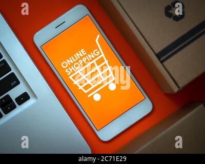 Online-Shopping-Konzept. Nahaufnahme Wörter 'Online Shopping' und Warenkorb-Symbol auf orangefarbenem Hintergrund auf Smartphone-Bildschirm und Laptop-Computer und par Stockfoto