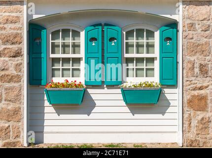 Teilweise Front außen von weißen Hütte mit blauem Fensterläden und Fensterboxen mit roten und weißen Impatiens Blumen Stockfoto