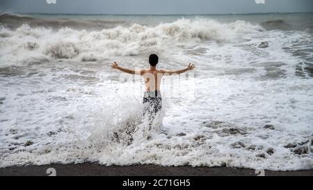 Antalya - Türkei - 17. Oktober 2013: Junger Mann steht gegen die Meereswellen mit Spritzern bei bewölktem Sturm Stockfoto