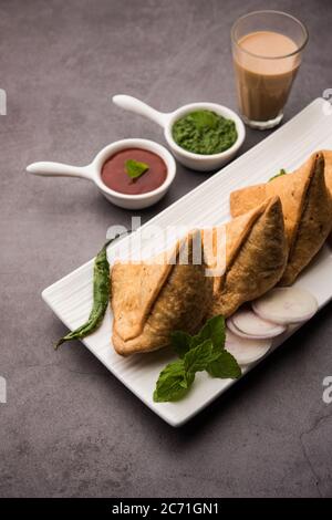 Samosa - Gebratenes Gebäck in Dreieckform mit herzhafter Füllung, beliebte indische Teezeit-Snacks, serviert mit grünem Chutney und Tomatenketchup Stockfoto