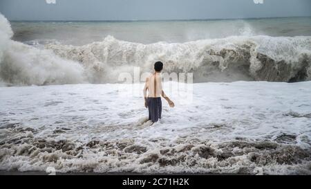 Antalya - Türkei - 17. Oktober 2013: Junger Mann steht gegen die Meereswellen mit Spritzern bei bewölktem Sturm Stockfoto