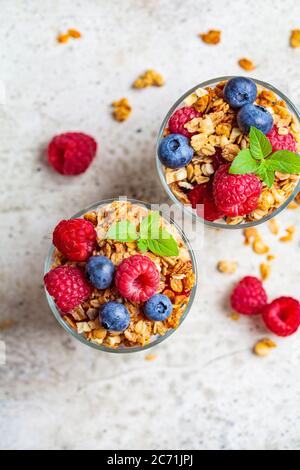 Joghurt-Parfait mit Granola, Himbeeren und Heidelbeeren in Gläsern, heller Hintergrund. Gesundes Frühstückskonzept. Stockfoto