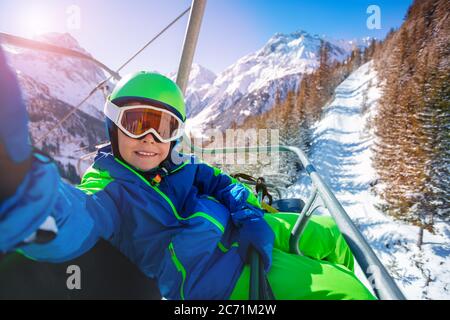 Niedlicher kleiner Junge nehmen Selfie auf dem Ski-Char-Lift im Sport-Outfit mit Berg auf dem Hintergrund sitzen Stockfoto