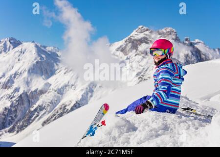 Happy junge Mädchen in hellen Sport-Outfit sitzen auf dem Schneehaufen in den Berg über hohe Gipfel Blick zurück zur Kamera Stockfoto