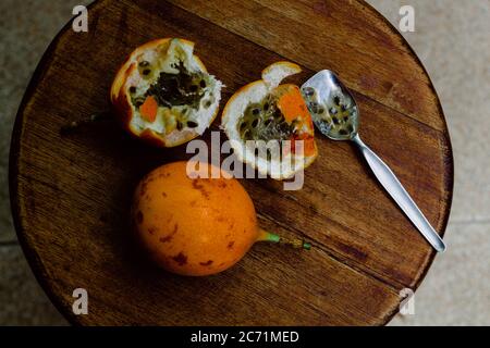 Mehrere Granadillas auf einem Holzteller angeordnet öffnen und mit einem Löffel, der das Innere des Produkts zeigt geschlossen Stockfoto
