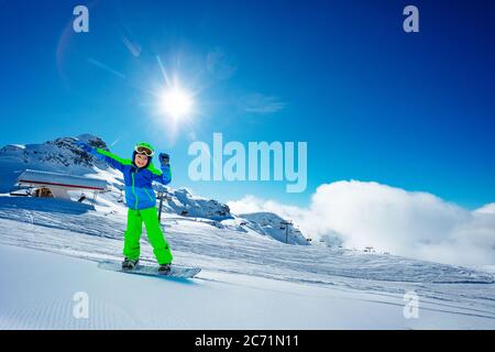 Portrait eines Jungen auf Snowboard Bewegen Sie schnell bergab über Skilift, Berg und helle Sonne in blauen Himmel auf Hintergrund Stockfoto