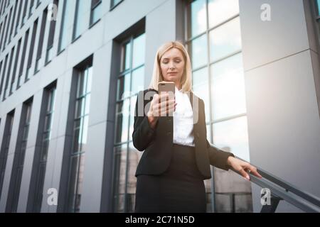 Elegante Geschäftsfrau mit einem Telefon in den Händen in der Nähe des Bürogebäudes Stockfoto