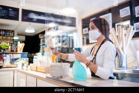 Junge Frau mit Gesichtsmaske arbeitet drinnen im Café, Desinfektion Zähler. Stockfoto
