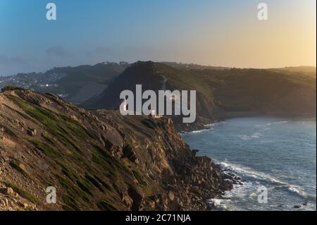 Blick auf die Landzungen am Eingang der Bucht São Martinho do Porto, mit dem Leuchtturm, bei Sonnenuntergang. Stockfoto