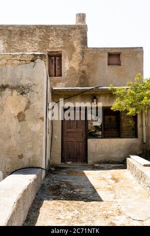 Altes braunes Haus mit Holztüren und Fenstern und einem alten Baum in Griechenland Stockfoto