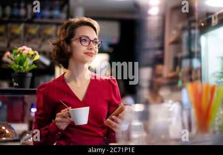Junge Frau mit Kaffee im Café, mit Smartphone. Stockfoto