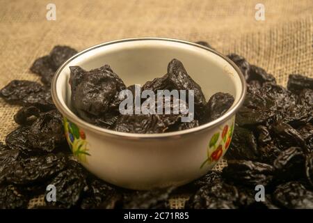Getrocknete Pflaumen in einer Metallschale und getrocknete Pflaumen auf einem Hintergrund von grobstrukturiertem Sackleinen verstreut. Nahaufnahme Stockfoto