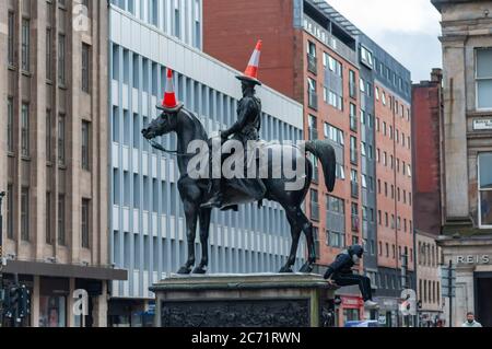 Glasgow, Schottland, Großbritannien. Juli 2020. Ein junger Mann mit Gesichtsmaske klettert die Duke of Wellington Statue hinauf, um drei Verkehrskegel auf den Duke und sein Pferd Kopenhagen zu legen. Kredit: Skully/Alamy Live Nachrichten Stockfoto