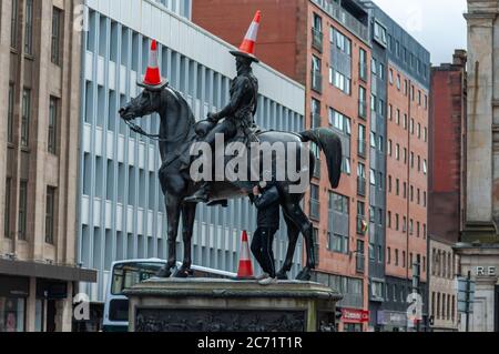 Glasgow, Schottland, Großbritannien. Juli 2020. Ein junger Mann mit Gesichtsmaske klettert die Duke of Wellington Statue hinauf, um drei Verkehrskegel auf den Duke und sein Pferd Kopenhagen zu legen. Kredit: Skully/Alamy Live Nachrichten Stockfoto