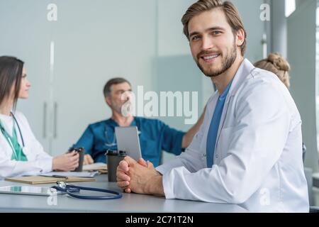 Porträt eines jungen Mannes Arzt in weißem Mantel sitzen in einem Treffen mit Geschäftsleuten verhandeln Krankenversicherung Stockfoto