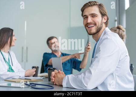 Porträt eines jungen Mannes Arzt in weißem Mantel sitzen in einem Treffen mit Geschäftsleuten verhandeln Krankenversicherung. Stockfoto