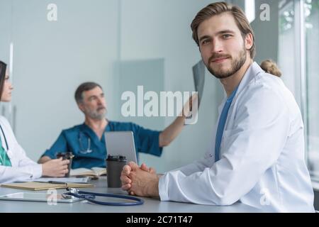 Porträt eines jungen Mannes Arzt in weißem Mantel sitzen in einem Treffen mit Geschäftsleuten verhandeln Krankenversicherung. Stockfoto