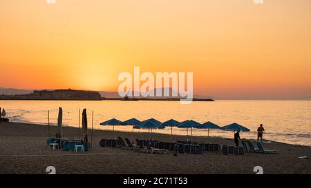 Sonnenuntergang über Sonnenschirm gefüllten Strand am Mittelmeer in Kreta, Griechenland Stockfoto