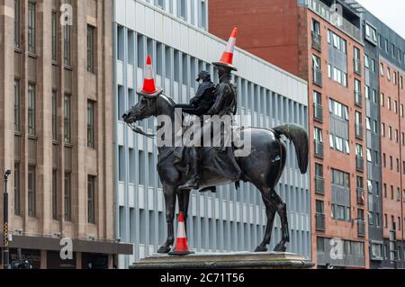 Glasgow, Schottland, Großbritannien. Juli 2020. Ein junger Mann mit Gesichtsmaske klettert die Duke of Wellington Statue hinauf, um drei Verkehrskegel auf den Duke und sein Pferd Kopenhagen zu legen. Kredit: Skully/Alamy Live Nachrichten Stockfoto