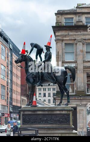 Glasgow, Schottland, Großbritannien. Juli 2020. Ein junger Mann mit Gesichtsmaske klettert die Duke of Wellington Statue hinauf, um drei Verkehrskegel auf den Duke und sein Pferd Kopenhagen zu legen. Kredit: Skully/Alamy Live Nachrichten Stockfoto