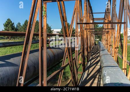 Alte rostige Eisenbrücke über den Fluss mit Dampfleitung. Wärmeversorgung. Industrieanlagen. Stockfoto